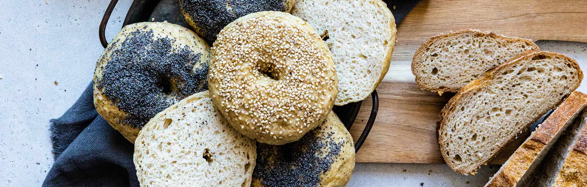 Des bagels sans gluten et des tranches de pain sans gluten Piaf déposés sur une planche en bois